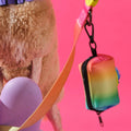 Rainbow köpek dışkı poşeti çantası, pembe arka planda kıvırcık tüylü köpeğin tasmasına asılı
